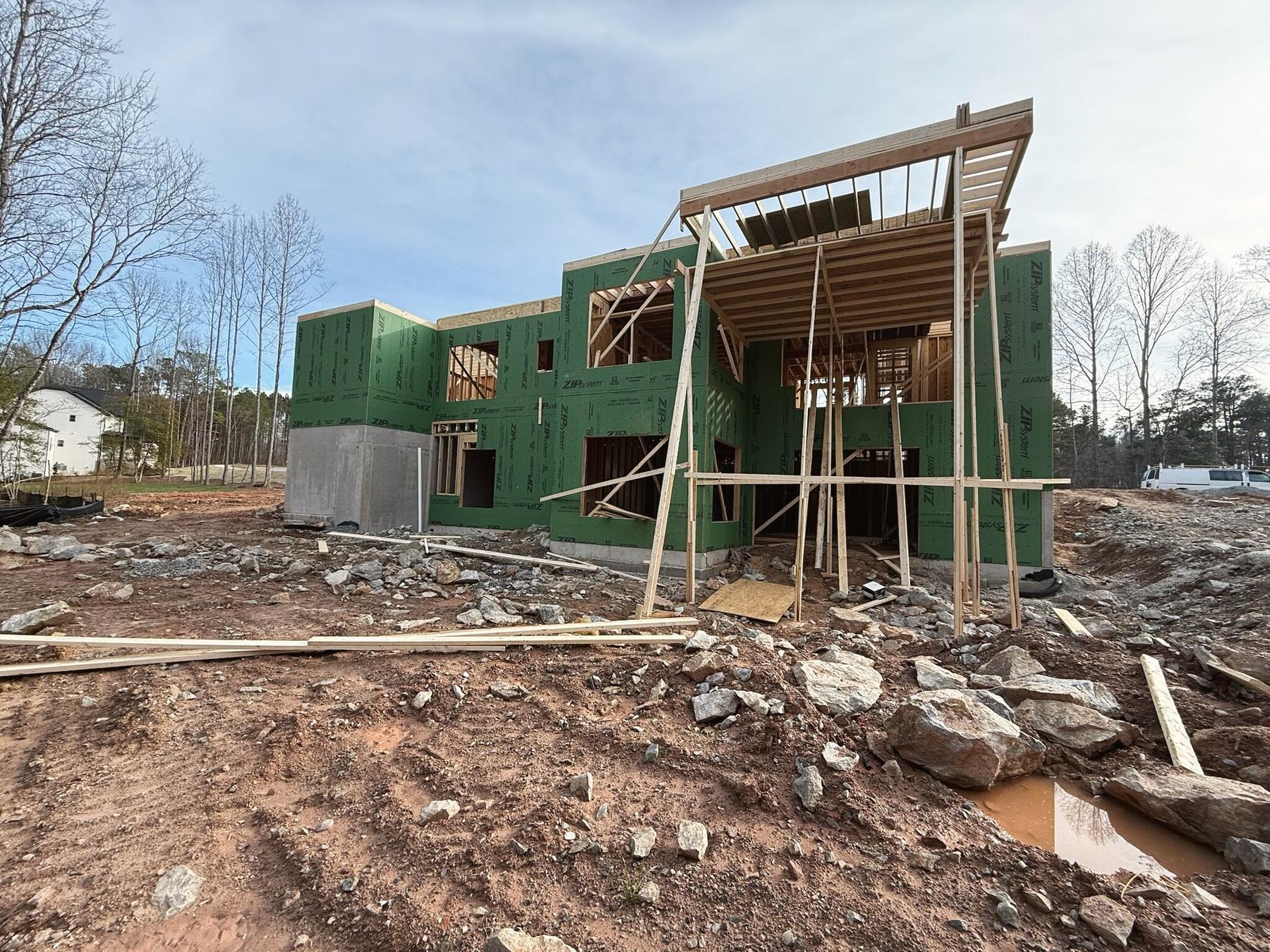 A two-story house under construction wrapped in green ZIP System panels, with scaffolding at the front