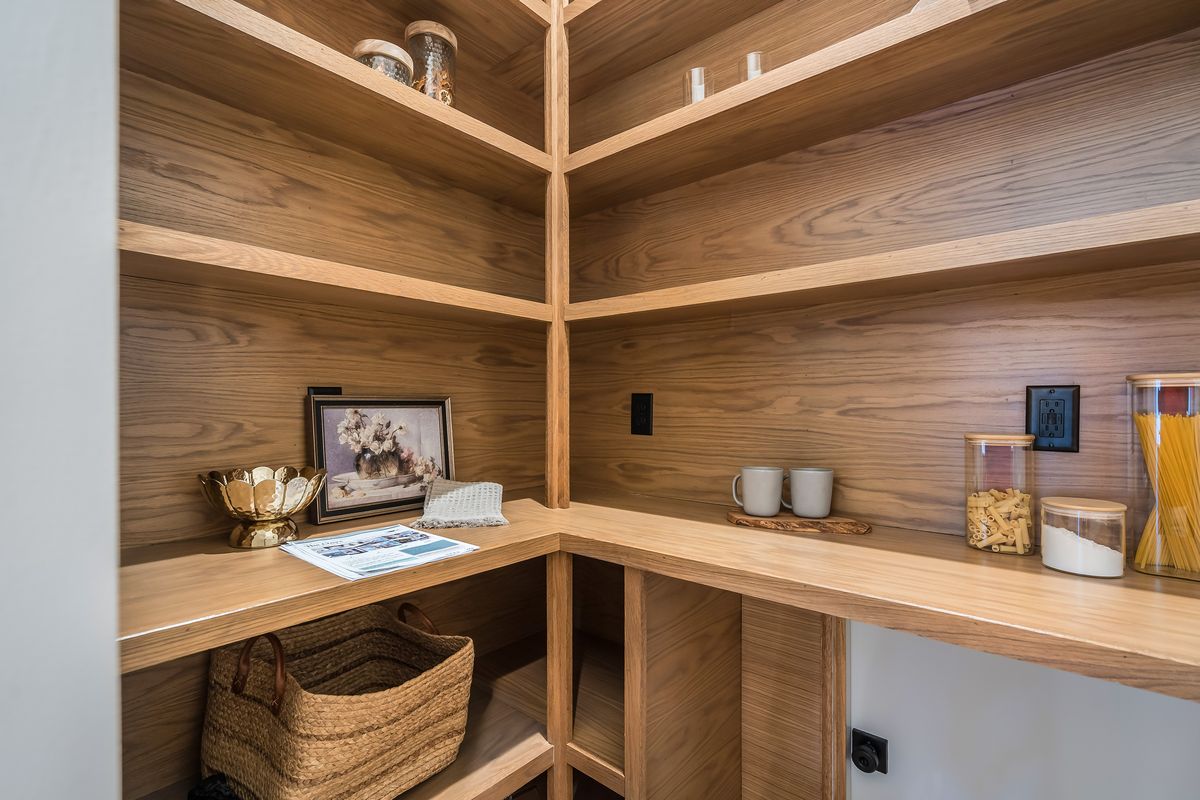 A pantry lined with wood shelving and a wood counter, with glass jars, mugs and a woven basket