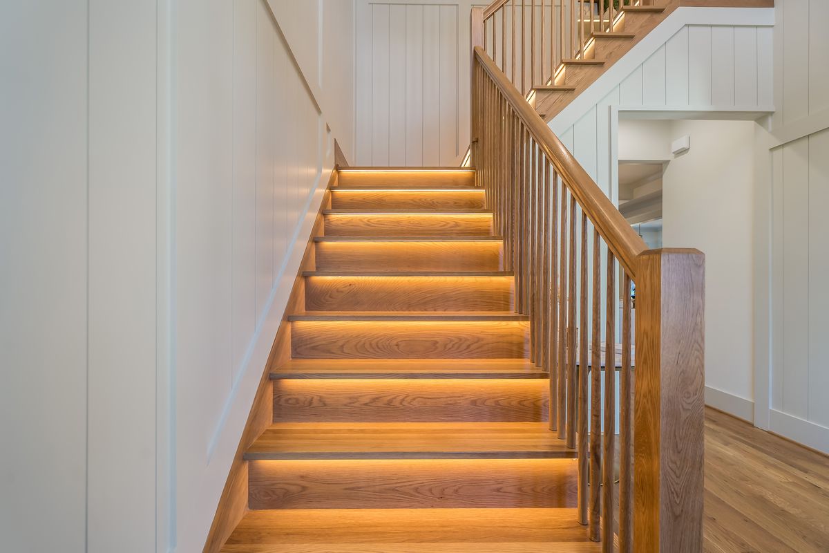 A wood stair with a light under each tread, a wood railing and white paneled walls