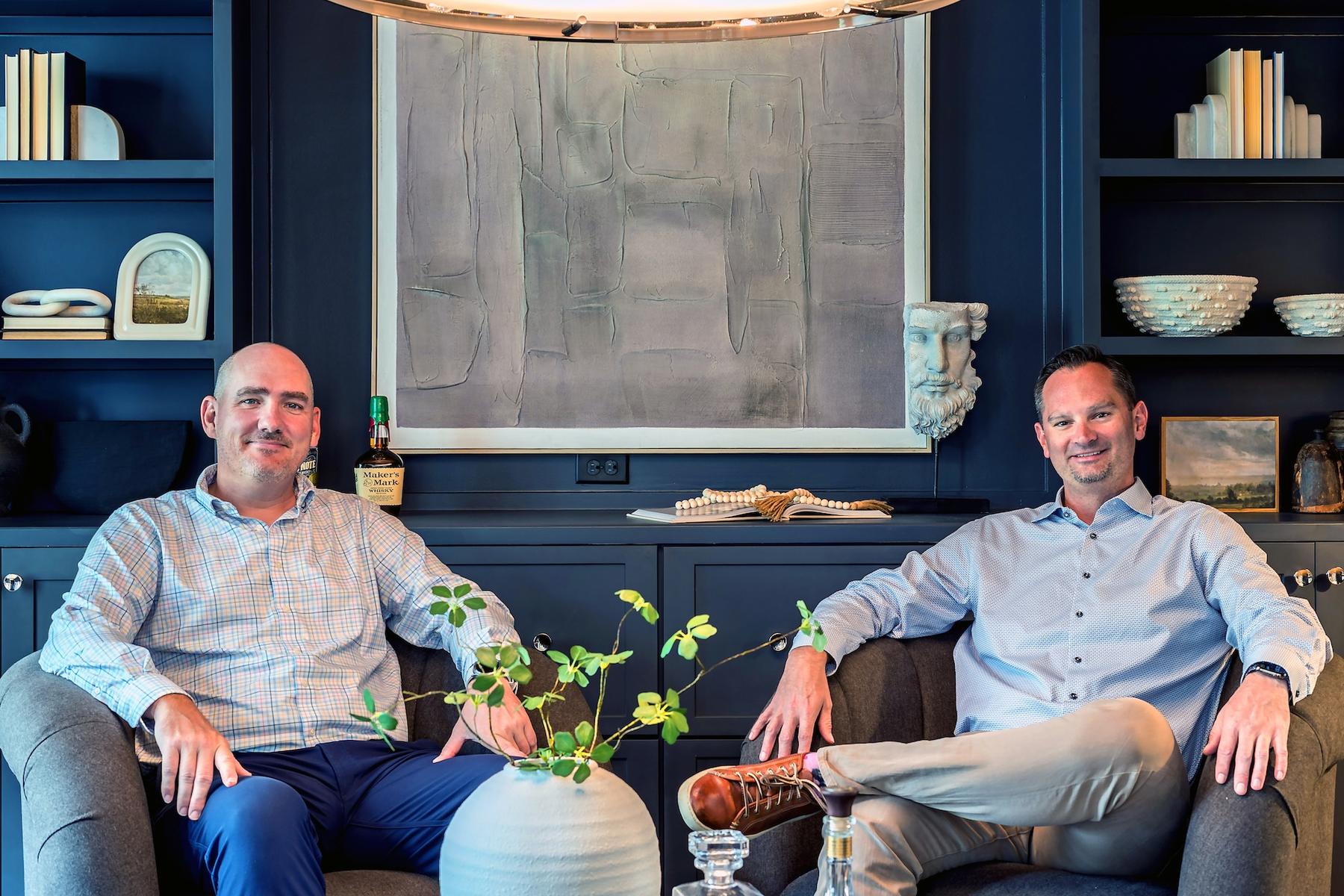Ken Godwin and Chris Schiavone seated in armchairs in front of navy built-in shelving