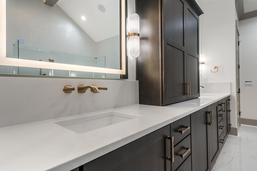Alabaster and brass sconce beside a backlit mirror in a Gemstone custom home